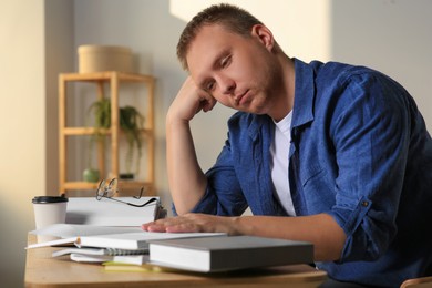 Tired man studying at wooden table indoors