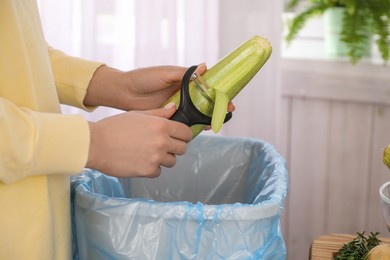 Photo of Woman peeling fresh zucchini above garbage bin indoors, closeup