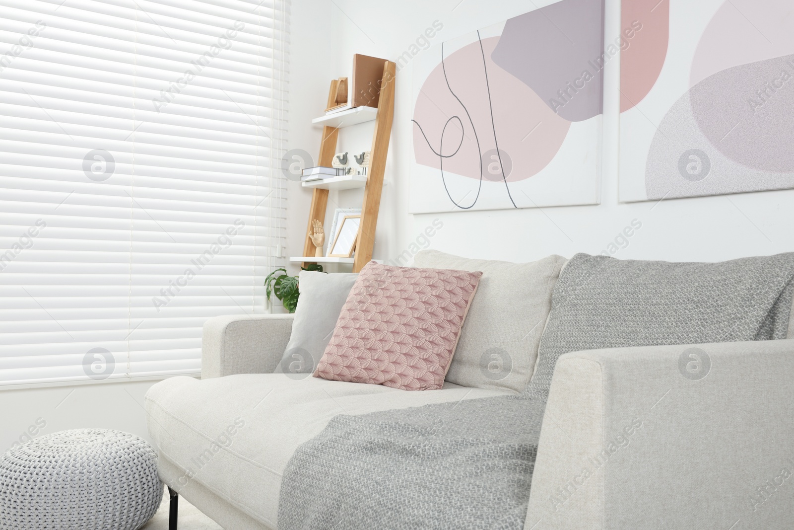 Photo of Stylish room interior with comfortable sofa, wooden shelf and pillows