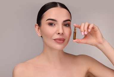 Beautiful young woman holding skincare ampoule on grey background