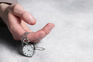 Man holding chain with elegant pocket watch at grey textured table, closeup. Space for text