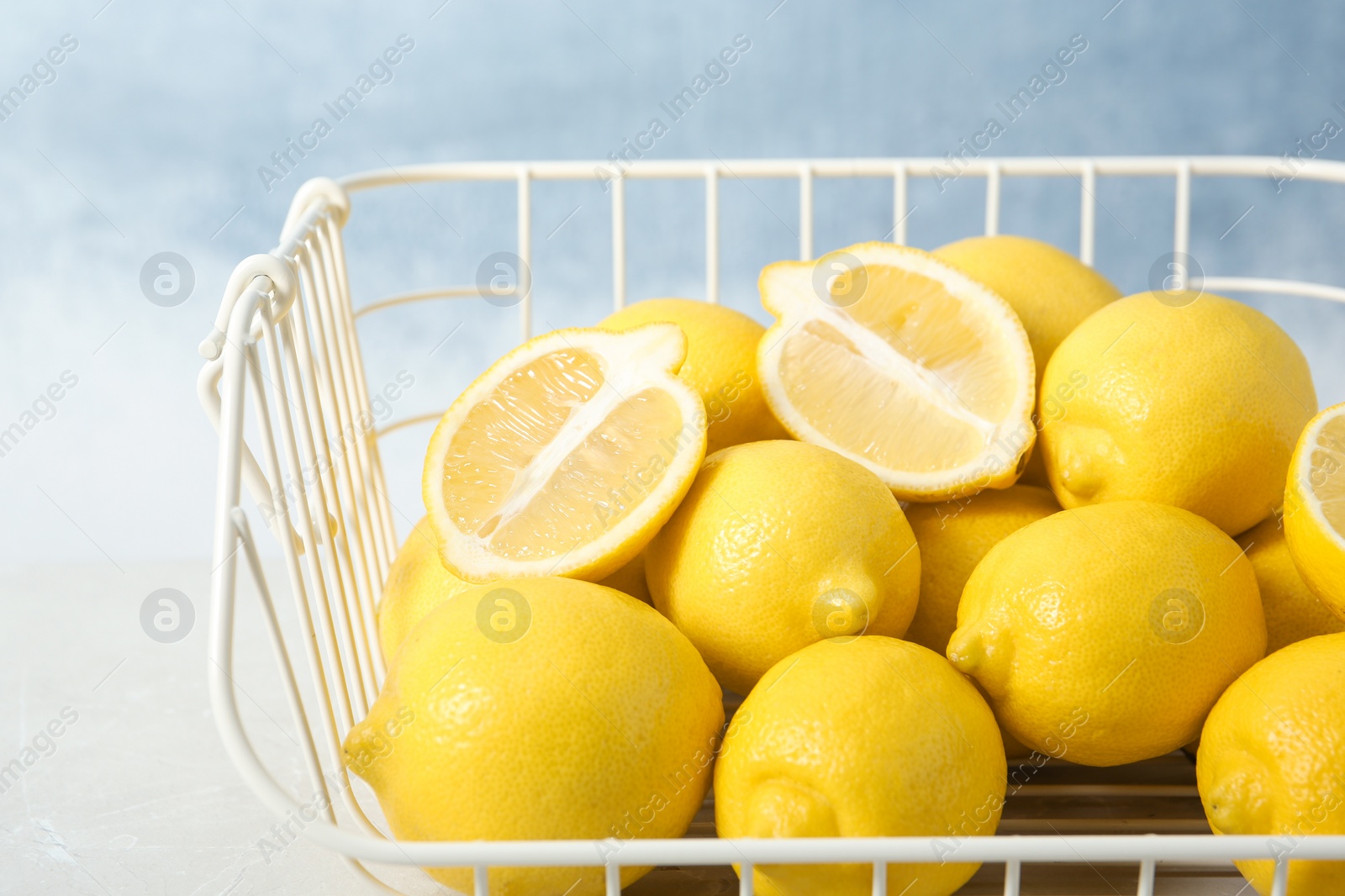 Photo of Wire basket with lemons on table against color background