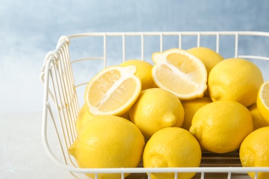 Wire basket with lemons on table against color background