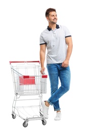 Young man with empty shopping cart on white background