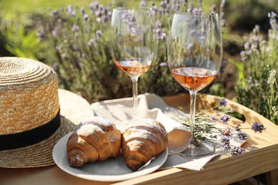 Photo of Plate with croissants and glasses of wine on wooden tray in lavender field