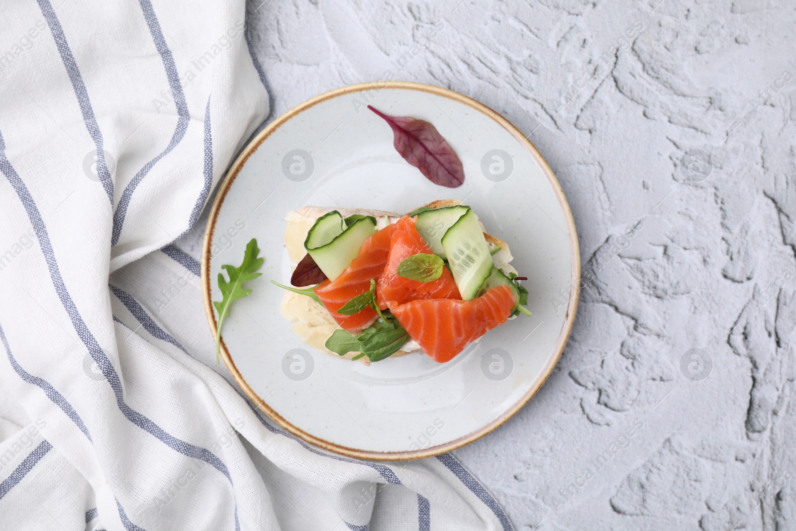 Photo of Tasty bruschetta with salmon, cucumbers and herbs on white textured table, top view