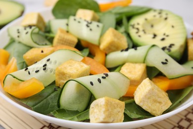 Photo of Bowl of tasty salad with tofu and vegetables on bamboo mat, closeup