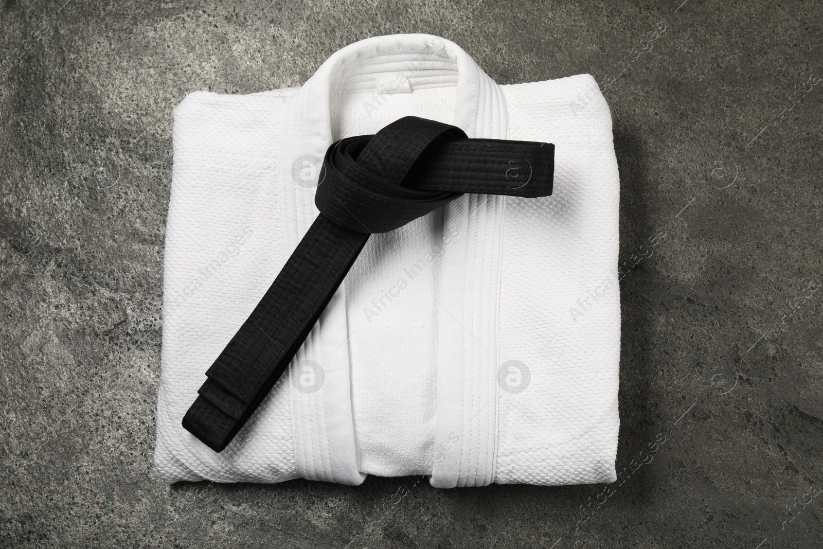 Photo of Black karate belt and white kimono on gray textured background, top view