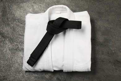 Black karate belt and white kimono on gray textured background, top view