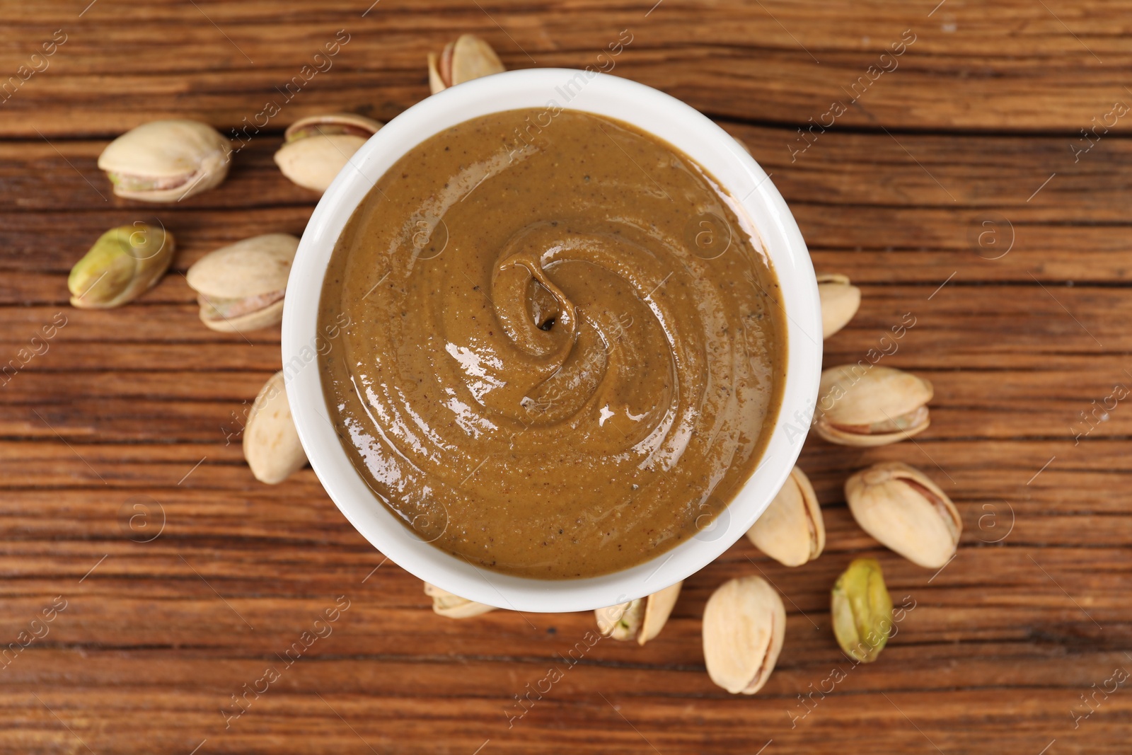 Photo of Delicious nut butter in bowl and pistachios on wooden table, top view