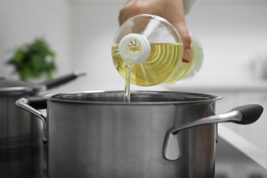 Woman pouring cooking oil from bottle into pot in kitchen, closeup