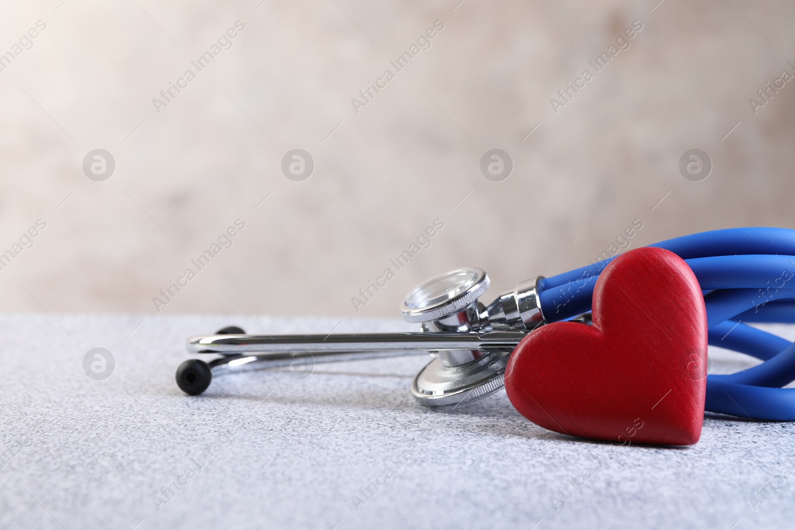 Photo of Stethoscope and red heart on grey stone table. Space for text