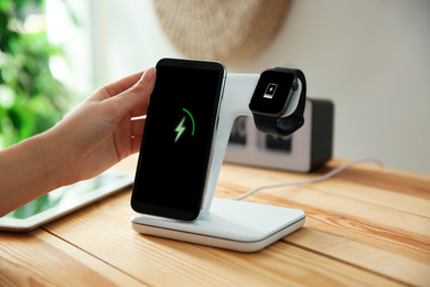 Woman putting mobile phone onto wireless charger at wooden table, closeup. Modern workplace accessory