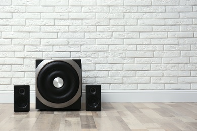 Photo of Modern powerful audio speaker system on floor near white brick wall. Space for text