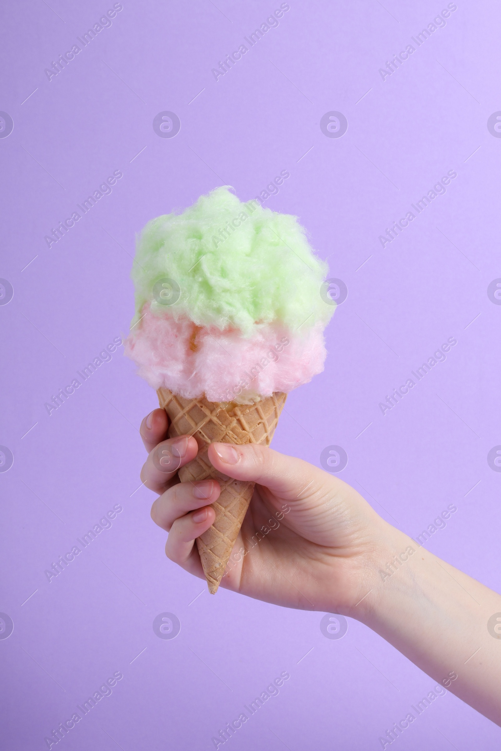 Photo of Woman holding waffle cone with cotton candy on violet background, closeup