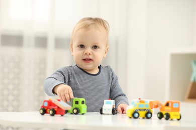 Children toys. Cute little boy playing with toy cars at white table in room