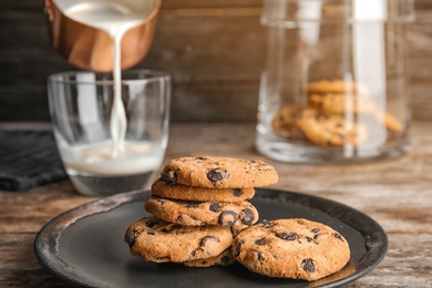 Photo of Plate with tasty chocolate chip cookies on wooden table