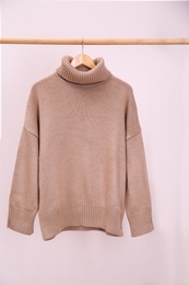 Stylish knitted sweater hanging on clothing rack near pink wall