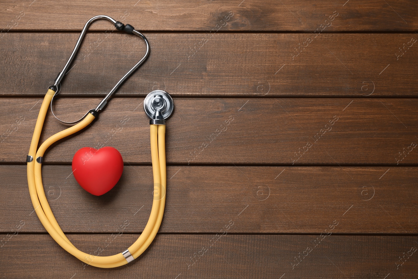 Photo of Stethoscope, red decorative heart and space for text on wooden background, flat lay. Cardiology concept