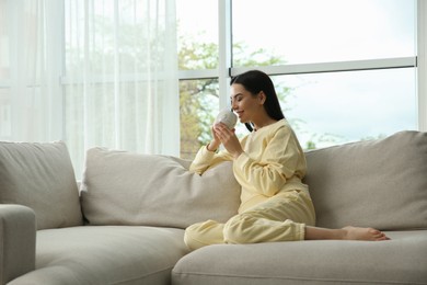 Photo of Young woman with cup of drink relaxing on sofa at home, space for text