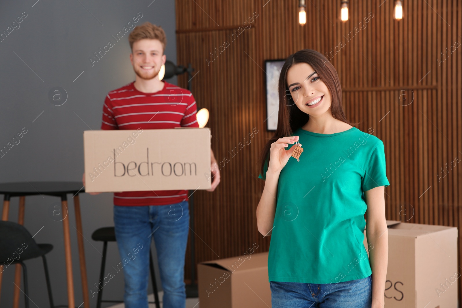 Photo of Young woman with key from new house and her boyfriend indoors. Moving day