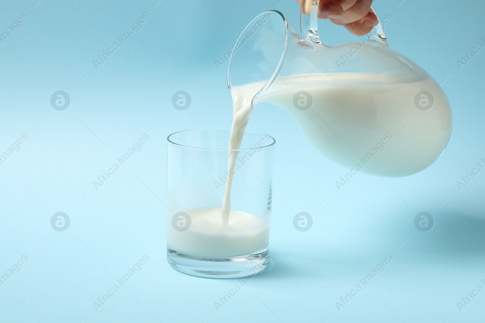 Photo of Woman pouring milk into glass on light blue background, closeup