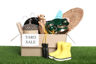 Photo of Sign Yard Sale written on box with different stuff on green grass against white background