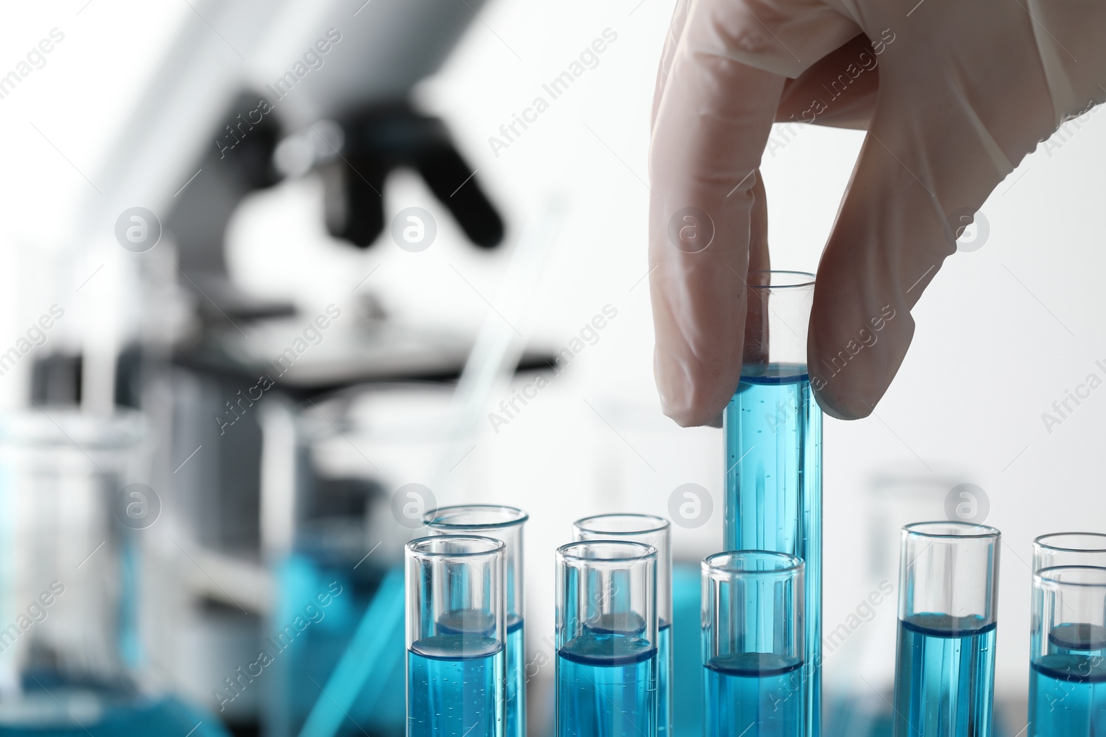 Photo of Scientist taking test tube with light blue liquid in laboratory, closeup