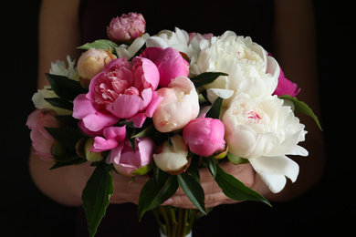 Woman with bouquet of beautiful peonies on black background, closeup