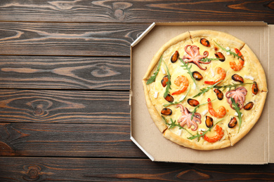 Delicious seafood pizza in cardboard box on wooden table, top view. Space for text