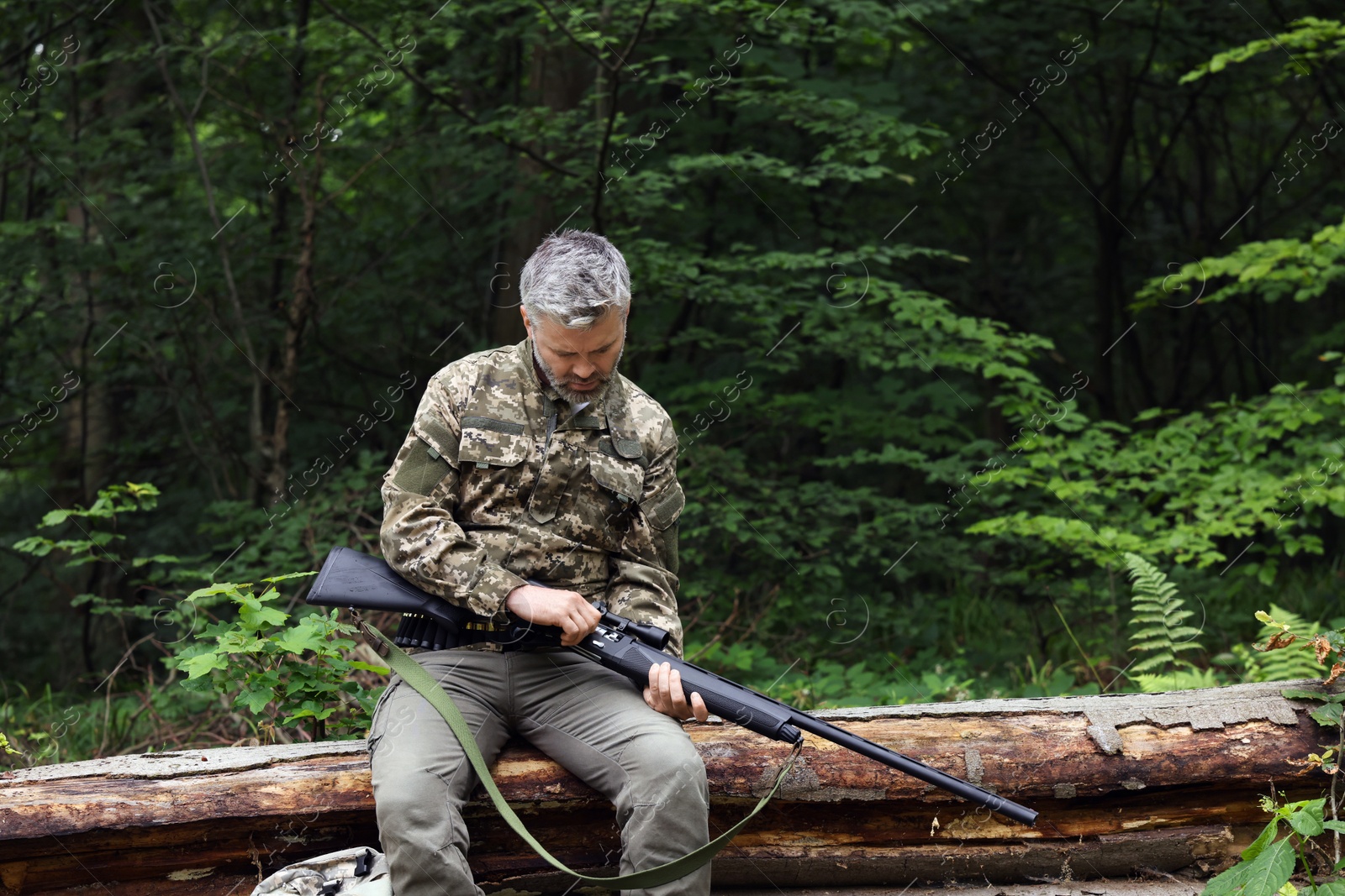 Photo of Man with hunting rifle sitting on fallen tree in forest. Space for text