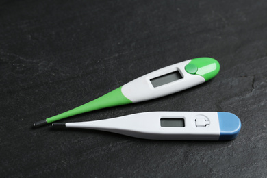 Photo of Modern digital thermometers on black slate background