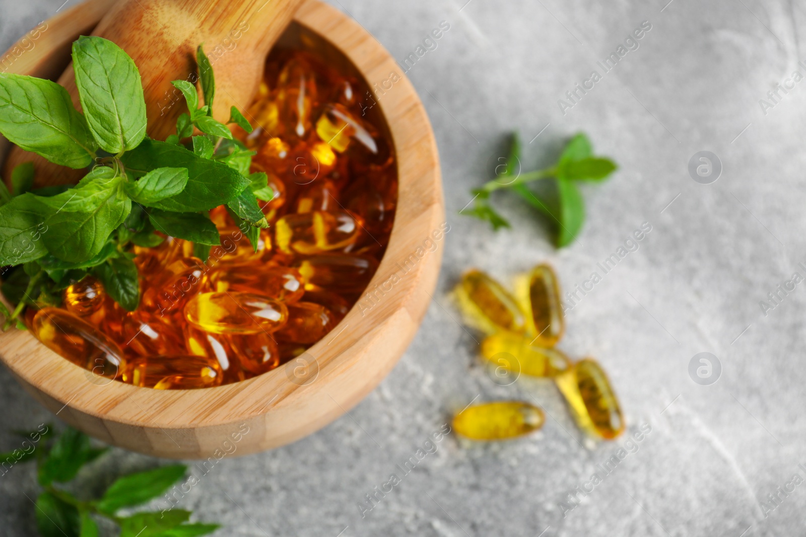 Photo of Wooden mortar with fresh green herbs and capsules on light grey table, top view