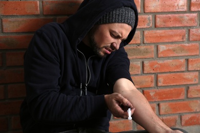 Photo of Male drug addict making injection near brick wall