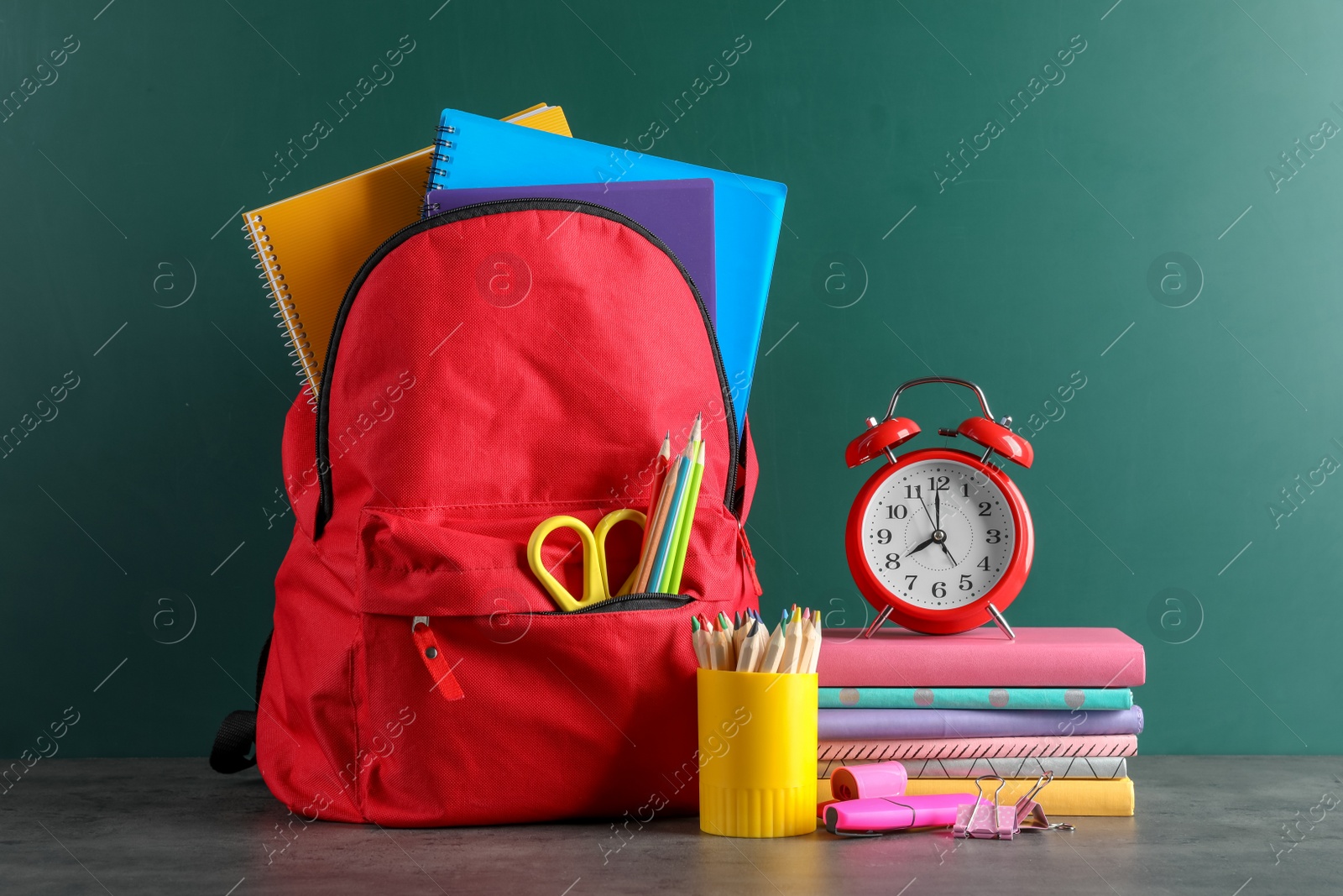 Photo of Backpack with school stationery on table against blackboard