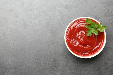 Photo of Delicious tomato ketchup and parsley in bowl on grey textured table, top view. Space for text