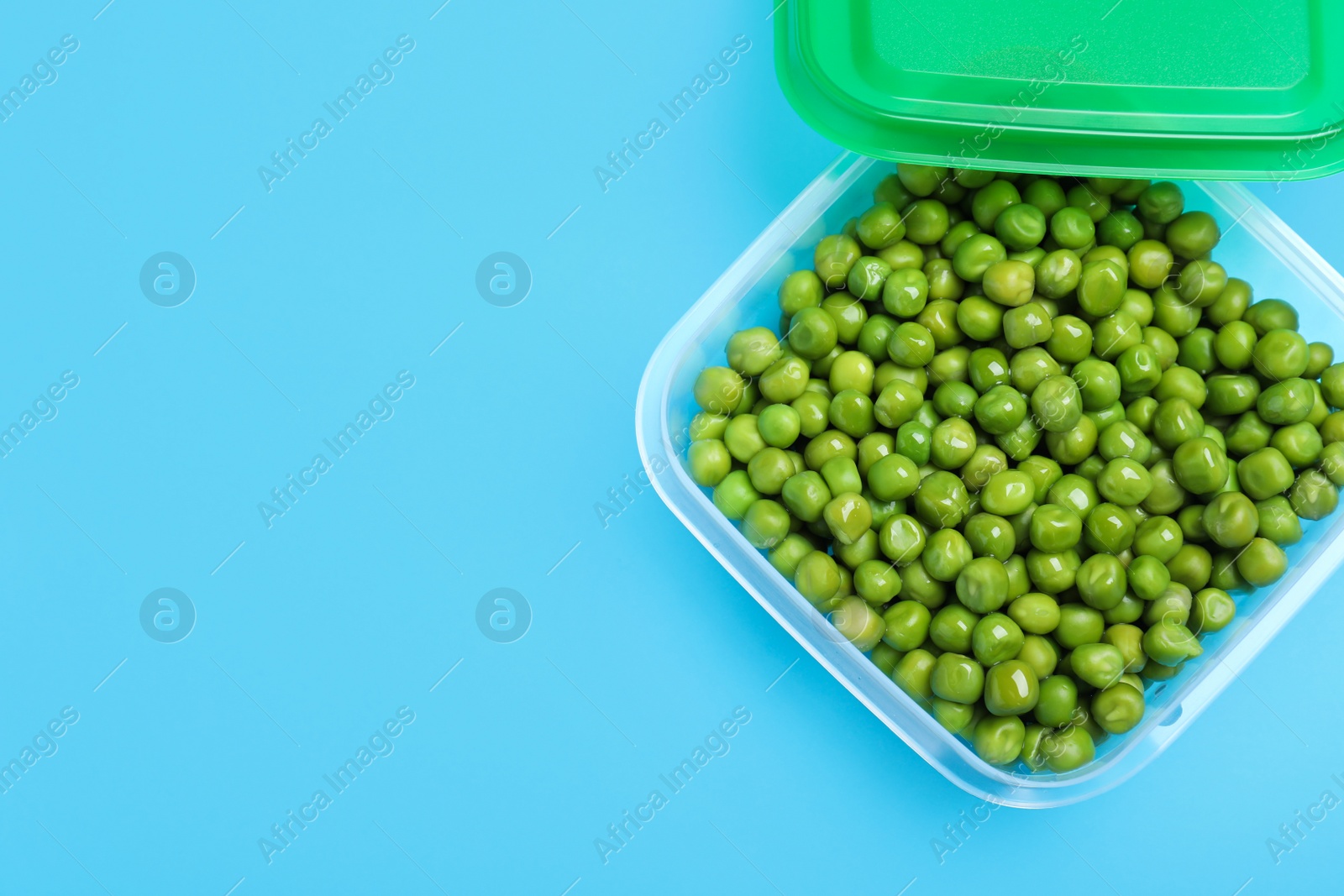 Photo of Fresh peas in glass container on light blue background, top view. Space for text