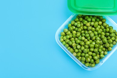 Photo of Fresh peas in glass container on light blue background, top view. Space for text