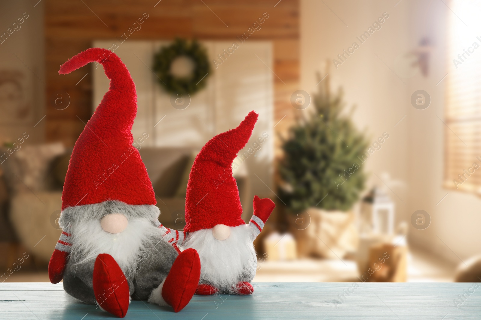 Image of Funny Christmas gnomes on turquoise wooden table in room with festive decorations. Space for text