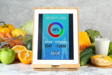 Photo of Tablet with weight loss calculator application and food products on white marble table