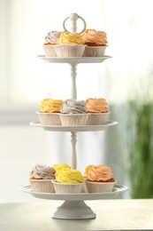 Photo of Dessert stand with tasty cupcakes on white table indoors, closeup