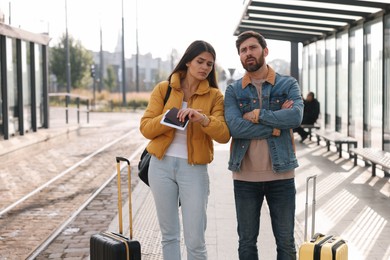 Photo of Being late. Worried couple with suitcases waiting at tram station outdoors