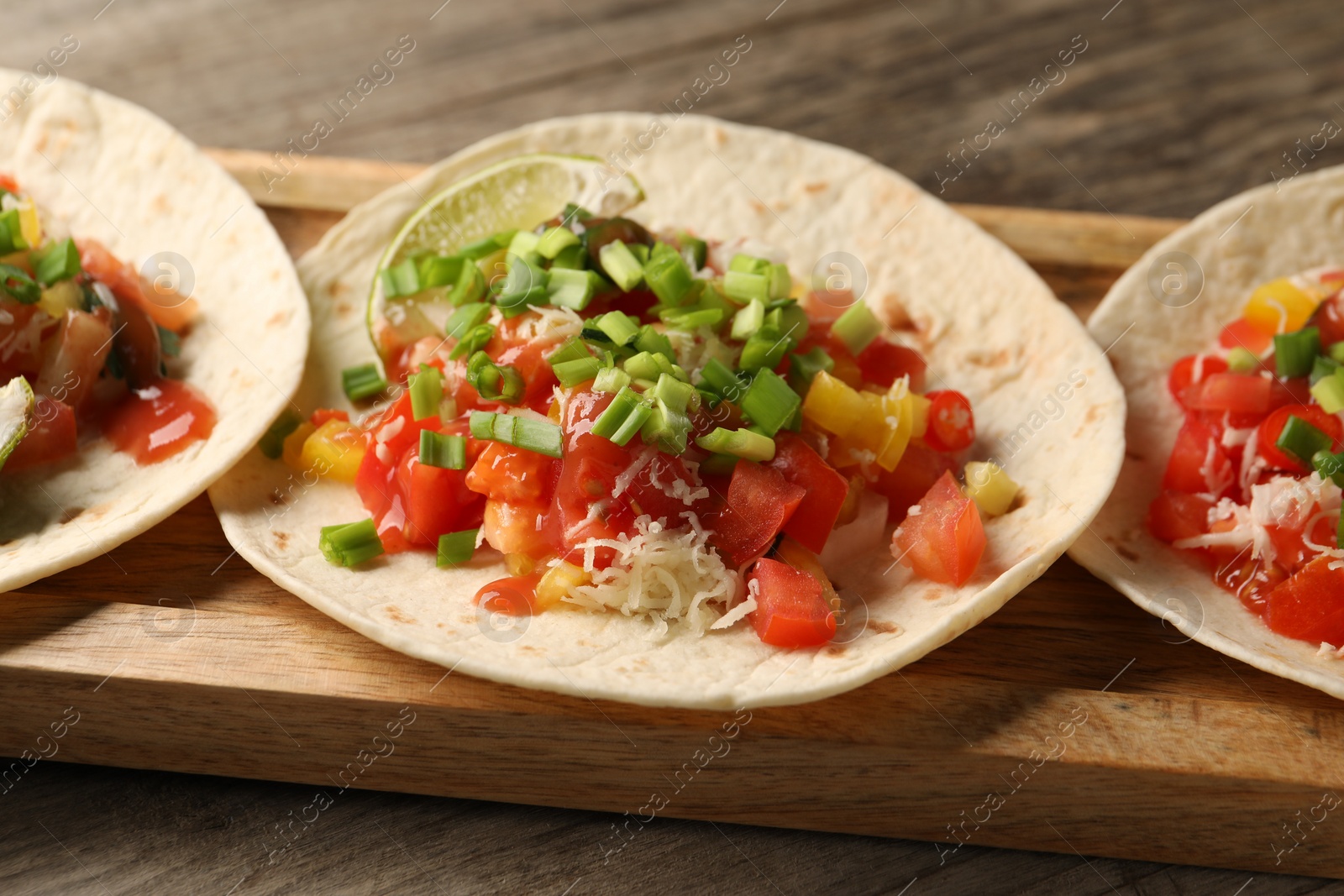 Photo of Delicious tacos with vegetables, green onion, lime and ketchup on wooden table, closeup