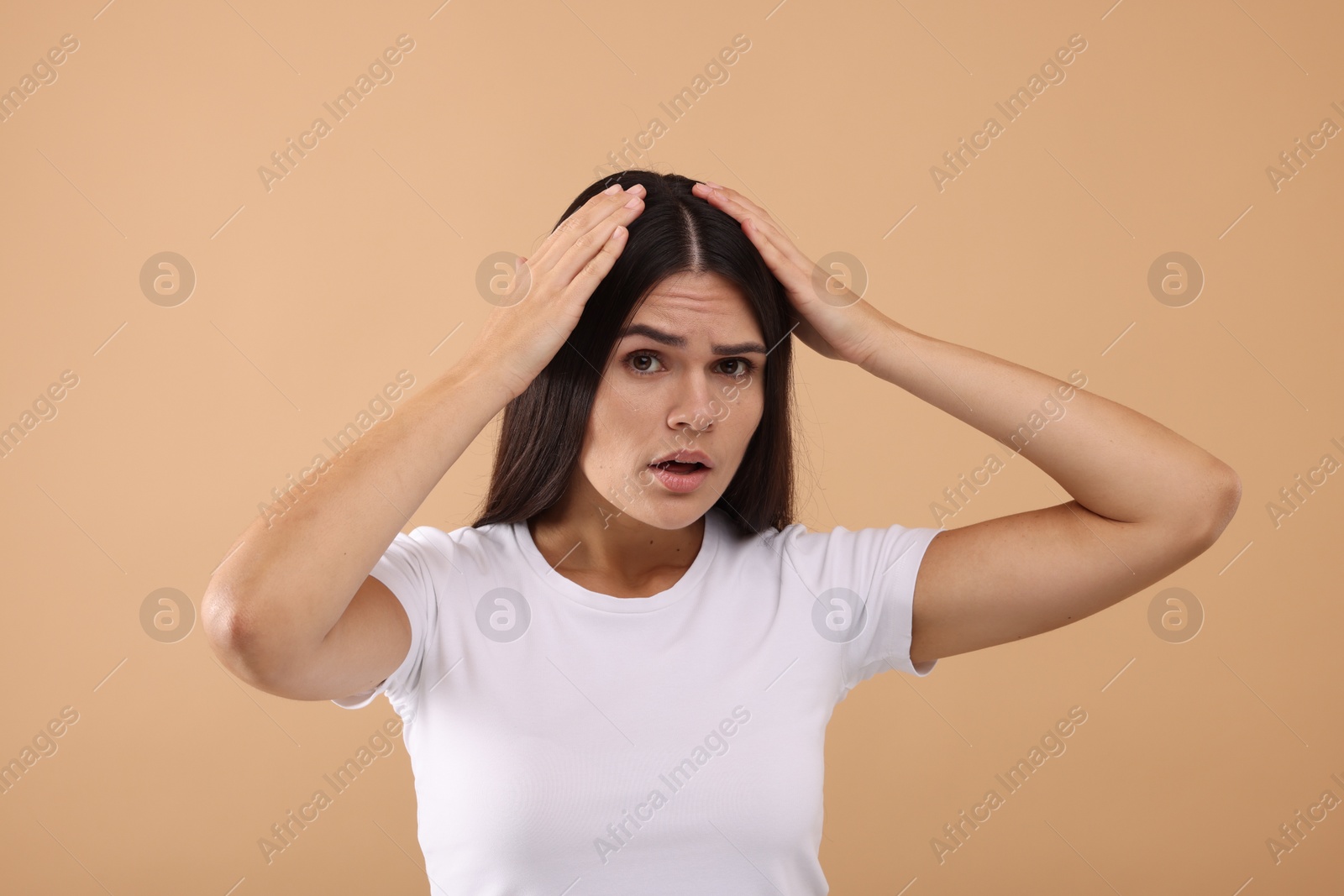 Photo of Emotional woman examining her hair and scalp on beige background