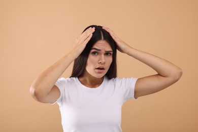 Photo of Emotional woman examining her hair and scalp on beige background