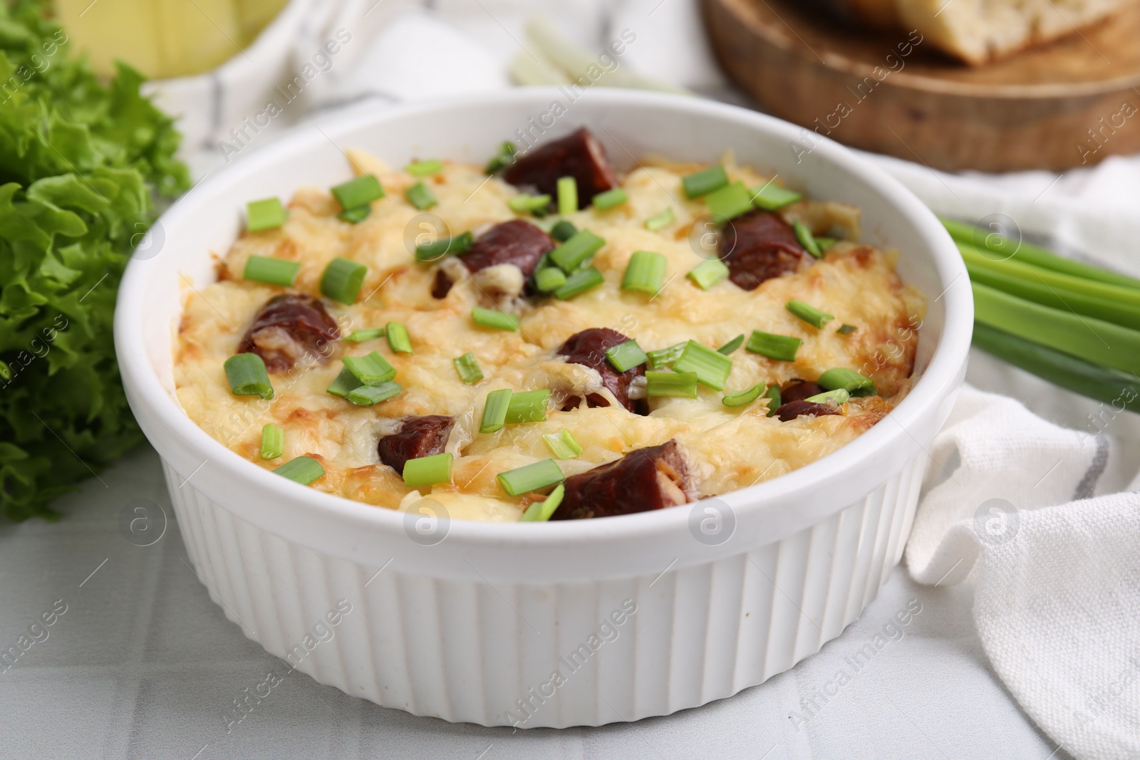 Photo of Tasty sausage casserole with green onion in baking dish on white tiled table, closeup