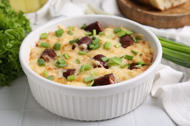 Photo of Tasty sausage casserole with green onion in baking dish on white tiled table, closeup