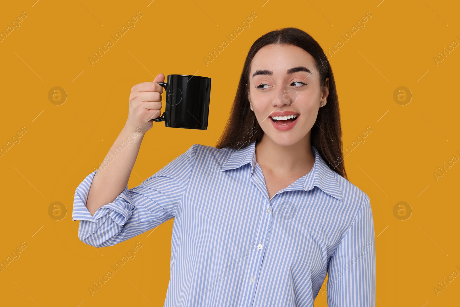 Photo of Happy young woman holding black ceramic mug on orange background