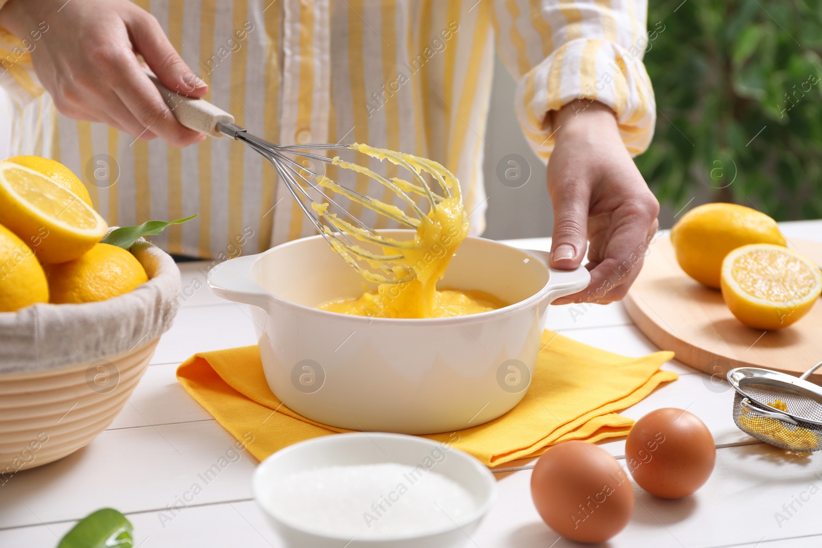 Photo of Woman cooking lemon curd at white wooden table, closeup