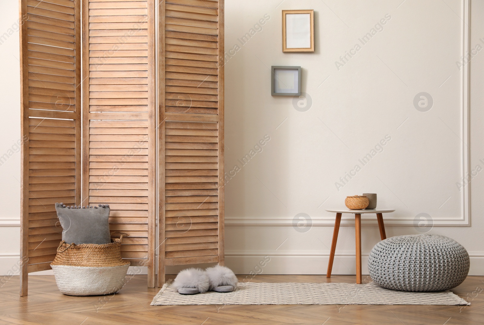 Photo of Folding screen, small table and knitted pouf near white wall in room. Interior design